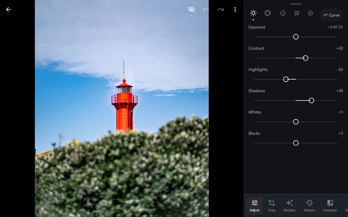 The editor on a wide screen: the red lighthouse on the left and, in a column on the right, the light adjustments with Contrast +22, Highlights -22 and Shadows +35.